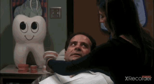 a woman is hugging a man in a dental chair with a tooth shaped pillow in the background