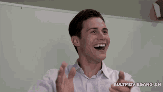 a man is laughing in front of a white board with kultmoviegang.ch written on it