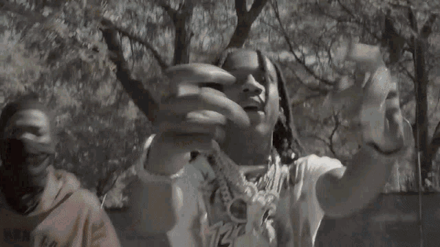 a man with dreadlocks is wearing a white shirt and gold chains around his neck