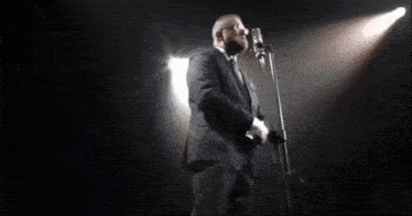 a man with glasses and a beard sings into a microphone .