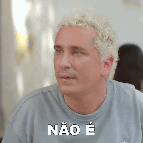 a man with curly blonde hair is wearing a grey shirt with the word não e on it