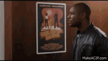 a man in a leather jacket is standing in front of a poster .