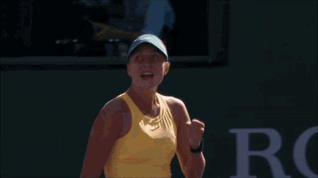 a woman wearing a yellow tank top and a blue hat is standing in front of a sign that says rolex