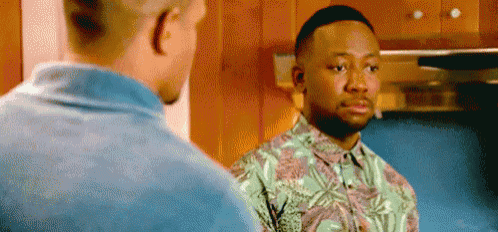 two men are standing next to each other in a kitchen . one of the men is wearing a hawaiian shirt .
