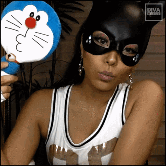 a woman wearing a cat mask is holding a stuffed doraemon toy