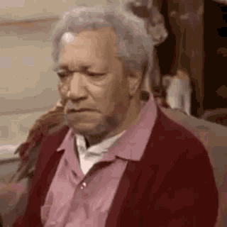 an elderly woman is sitting on a couch wearing glasses and a red sweater .