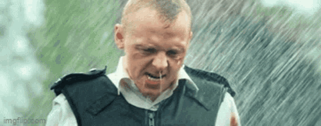 a man in a bullet proof vest is standing in the rain with his mouth open .