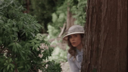a woman is peeking out from behind a tree .