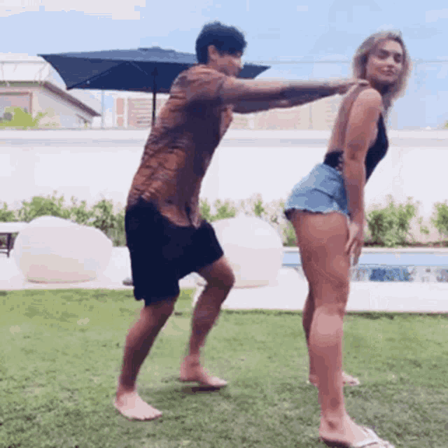 a man is touching a woman 's butt while standing on the grass in front of a pool .