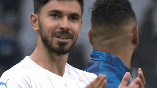 a man with a beard wears a white shirt with blue pumas on the front