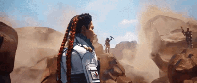 a woman with braids is standing on top of a rocky hill in the desert .