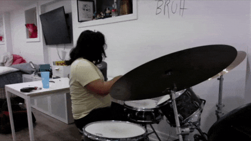 a woman is playing drums in front of a wall that has the word bruh written on it