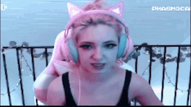 a woman wearing pink headphones with cat ears is sitting in front of a railing .