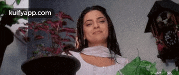 a woman in a white dress is standing in front of a potted plant and smiling .