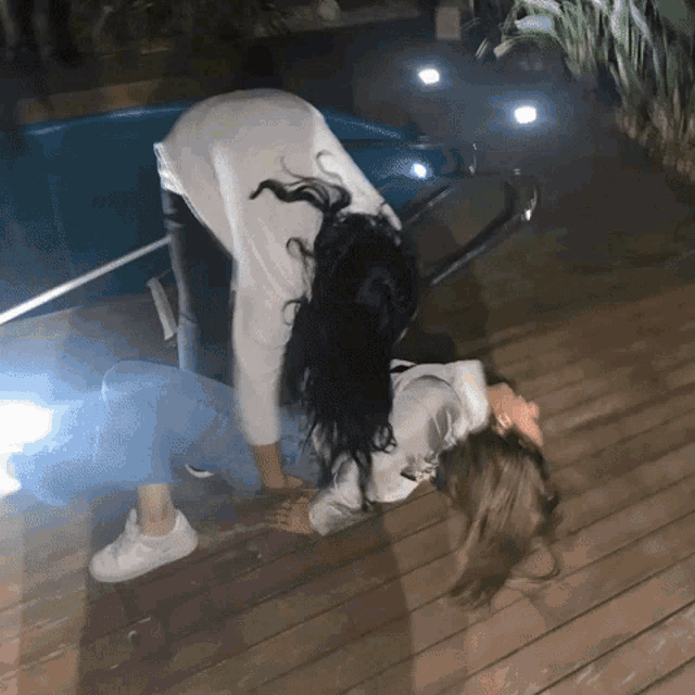 a woman laying on another woman 's back on a wooden deck