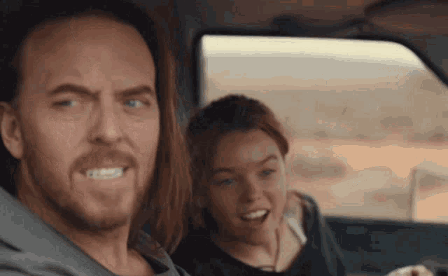 a man and woman are sitting in a car and the man is making a funny face
