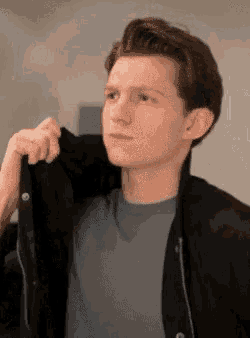 a young man is wearing a black jacket over his shoulder and a blue shirt .