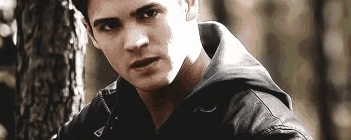 a man in a black leather jacket leaning against a tree