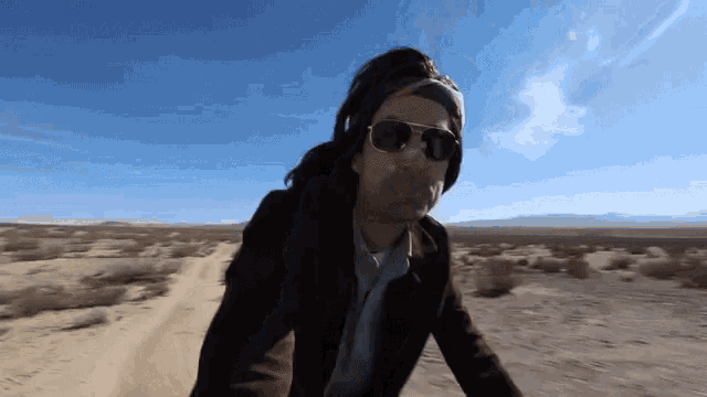 a man wearing sunglasses and a helmet is riding a bike on a dirt road in the desert