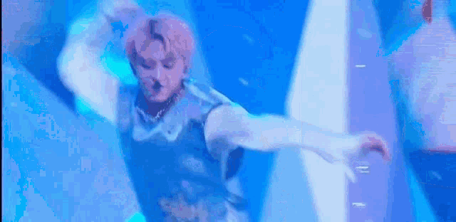 a man with pink hair is dancing on a stage in a blue light .