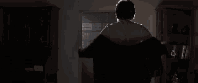 a man in a suit stands in a dark room in front of a bookcase