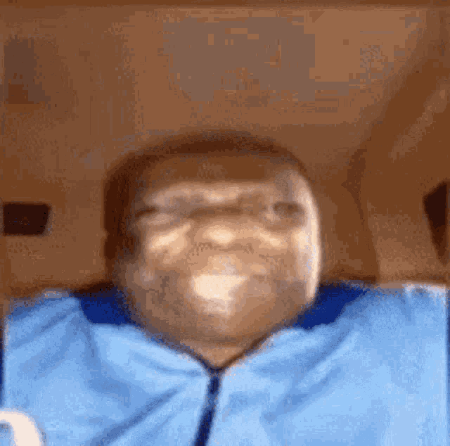 a man in a blue shirt is making a funny face while laying on a bed .