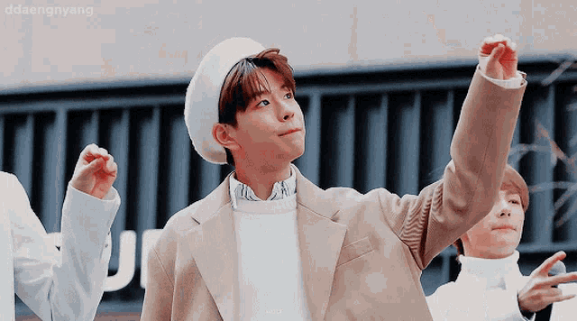 a boy wearing a white beret and a tan jacket is standing in front of a sign that says ddaengnyang