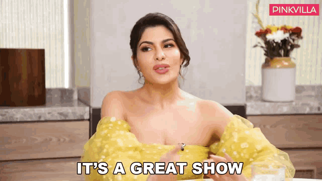 a woman in a yellow dress is sitting at a table and says it 's a great show