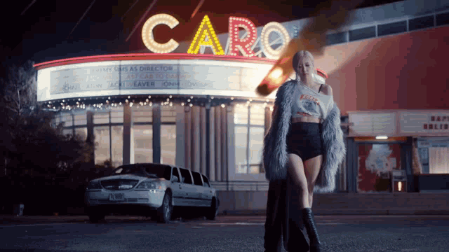 a woman in a fur coat stands in front of a caro theater