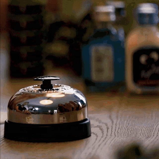 a silver bell sits on a wooden table in front of bottles of alcohol