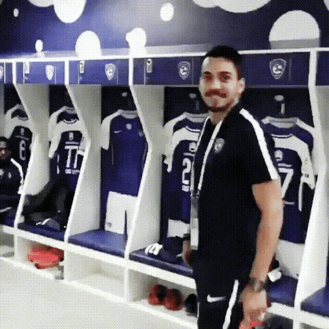 a man is standing in a locker room with jerseys hanging on the wall including one that has the number 17 on it