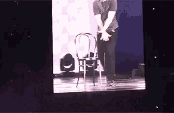 a man is standing next to a chair on a stage in front of a screen .
