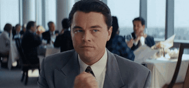 a man in a suit and tie is sitting at a table in a restaurant with other people .