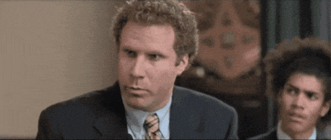 a man in a suit and tie is looking at the camera while another man looks on .