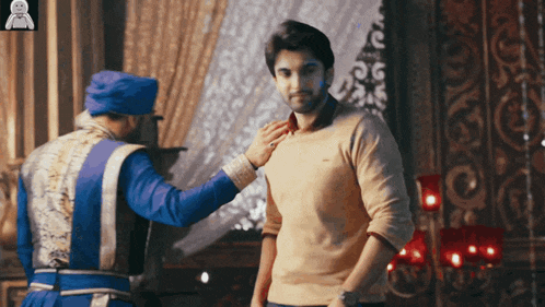 a man in a blue turban adjusts another man 's shirt