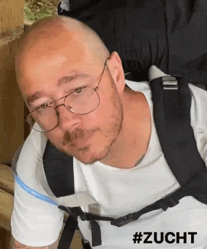 a man wearing glasses and a backpack has the hashtag #zucht on the bottom right