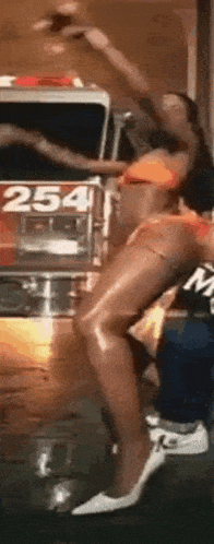 a woman in a bikini is dancing in front of a fire truck with the number 254 on it