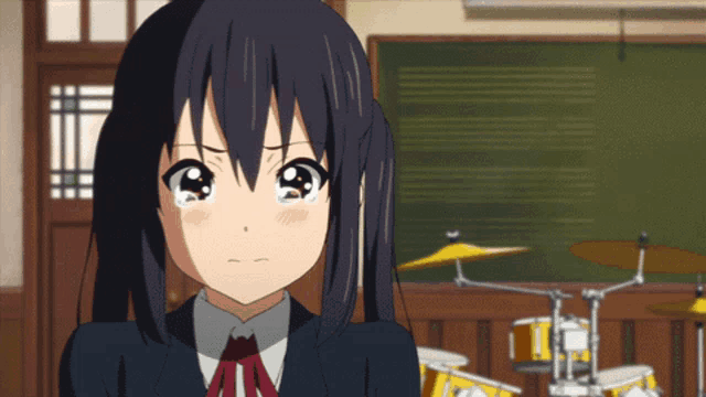 a girl in a school uniform is crying in front of drums