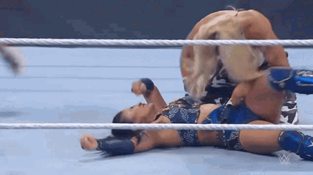 a woman is laying on the ground in a wrestling ring while another woman is standing on top of her .