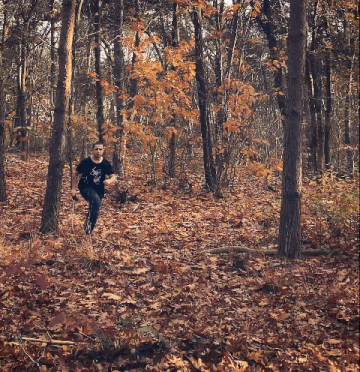 a man wearing a black shirt with a skull on it is running through a forest