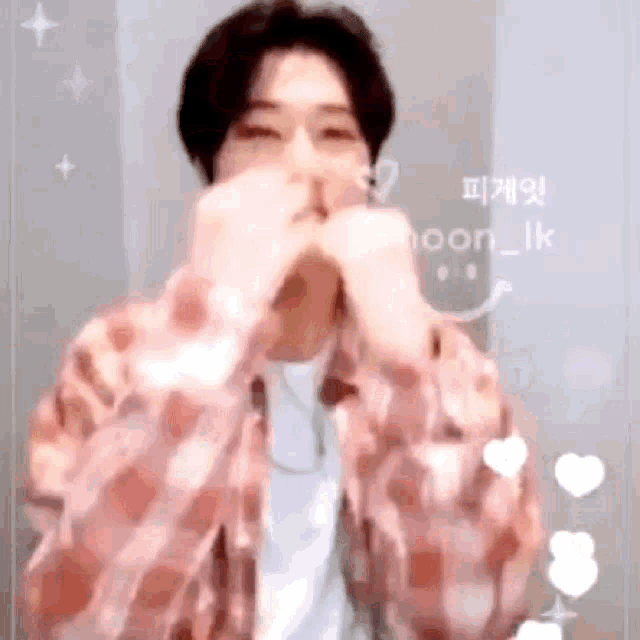 a man in a pink plaid shirt is making a heart shape with his hands .