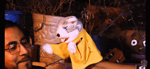 a man with glasses holds a stuffed animal with a yellow jacket on