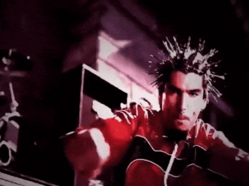 a man with dreadlocks is wearing a red and black jacket and waving at the camera .