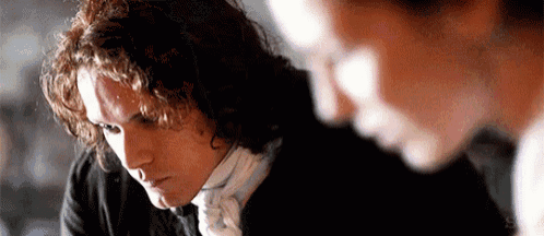 a man with curly hair is sitting next to another man in a room .