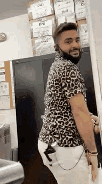 a man wearing a leopard print shirt and white pants is standing in a room with boxes on the wall .