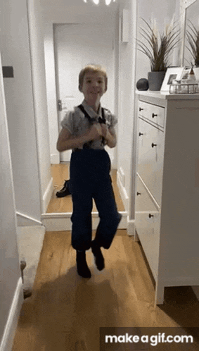 a young boy wearing suspenders is dancing in a hallway .