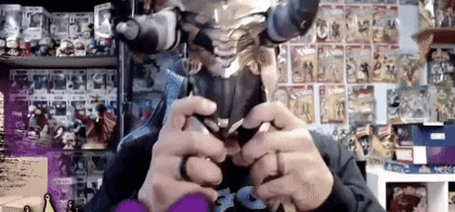a man wearing a mask is playing a video game in front of a wall filled with comics .