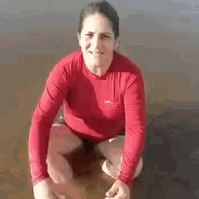 a woman in a red shirt is kneeling in the water and smiling .