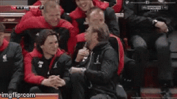 a group of people are sitting in a stadium watching a soccer game and a man is talking to another man