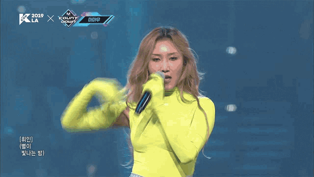 a woman in a yellow outfit is dancing on a stage in front of a screen that says k-la